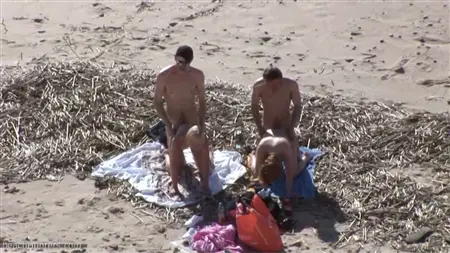 A crowd of guys on the beach lets in a circle of two prostitutes